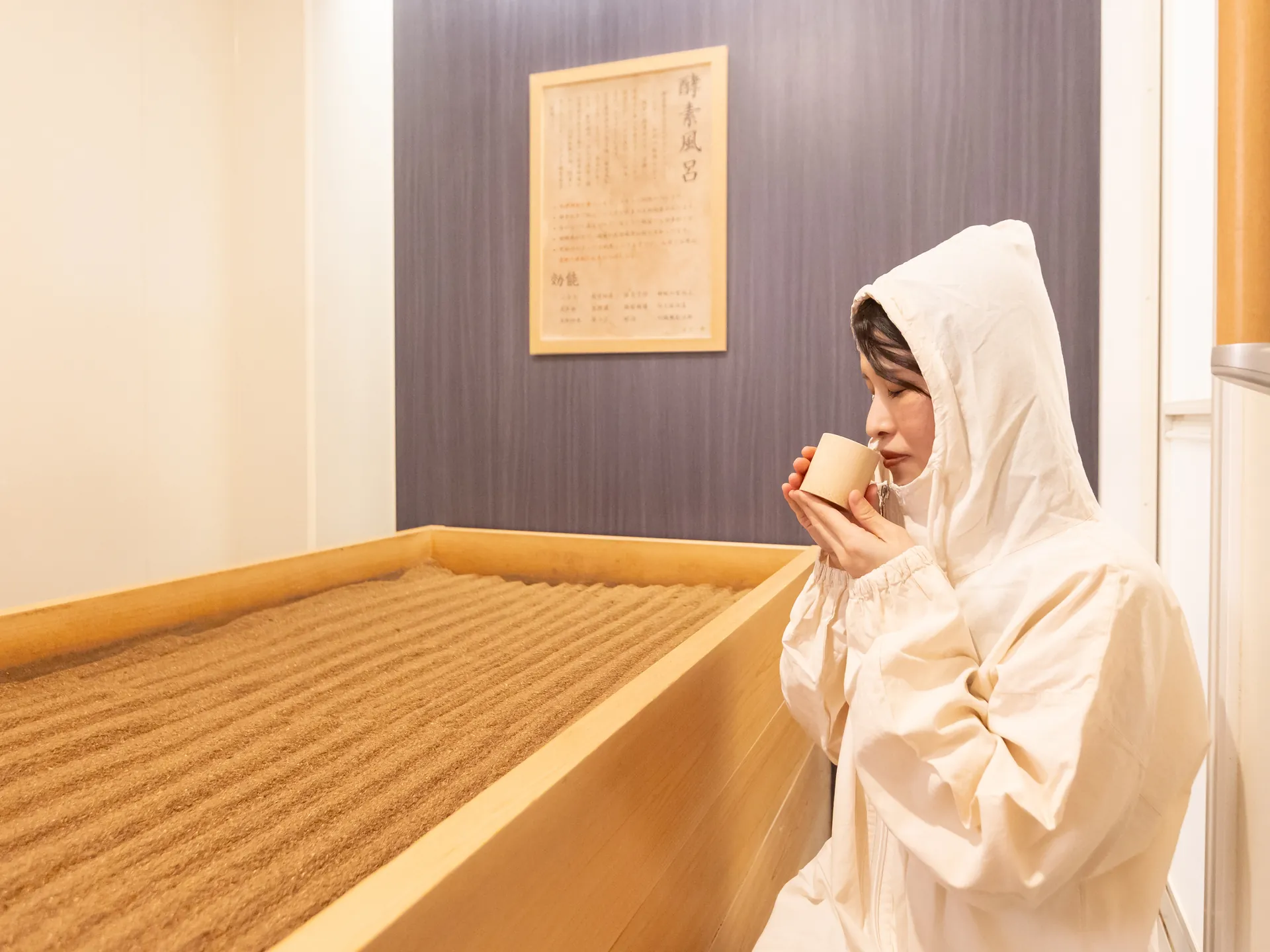 檜づくりの酵素風呂の縁に腰かけ、発酵ドリンクを飲むお客様